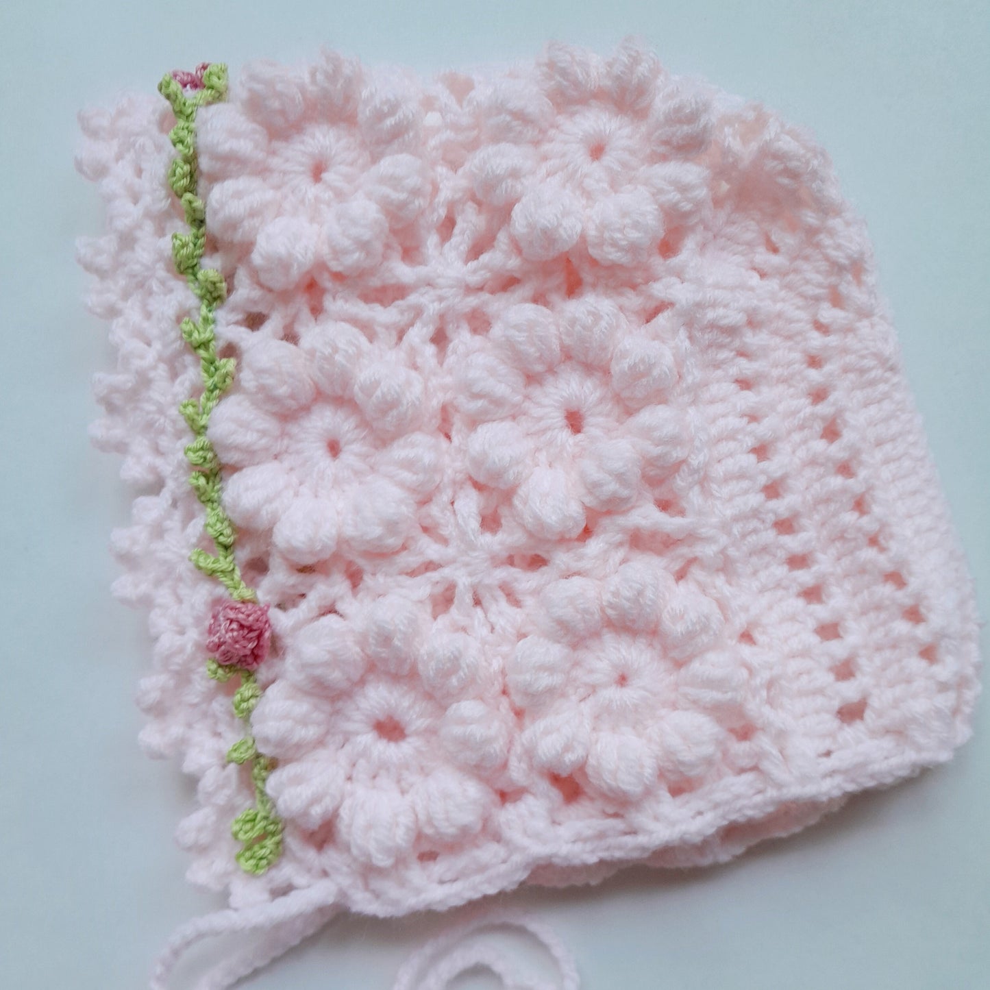 Pink crocheted baby bonnet with floral patterns on a light blue background