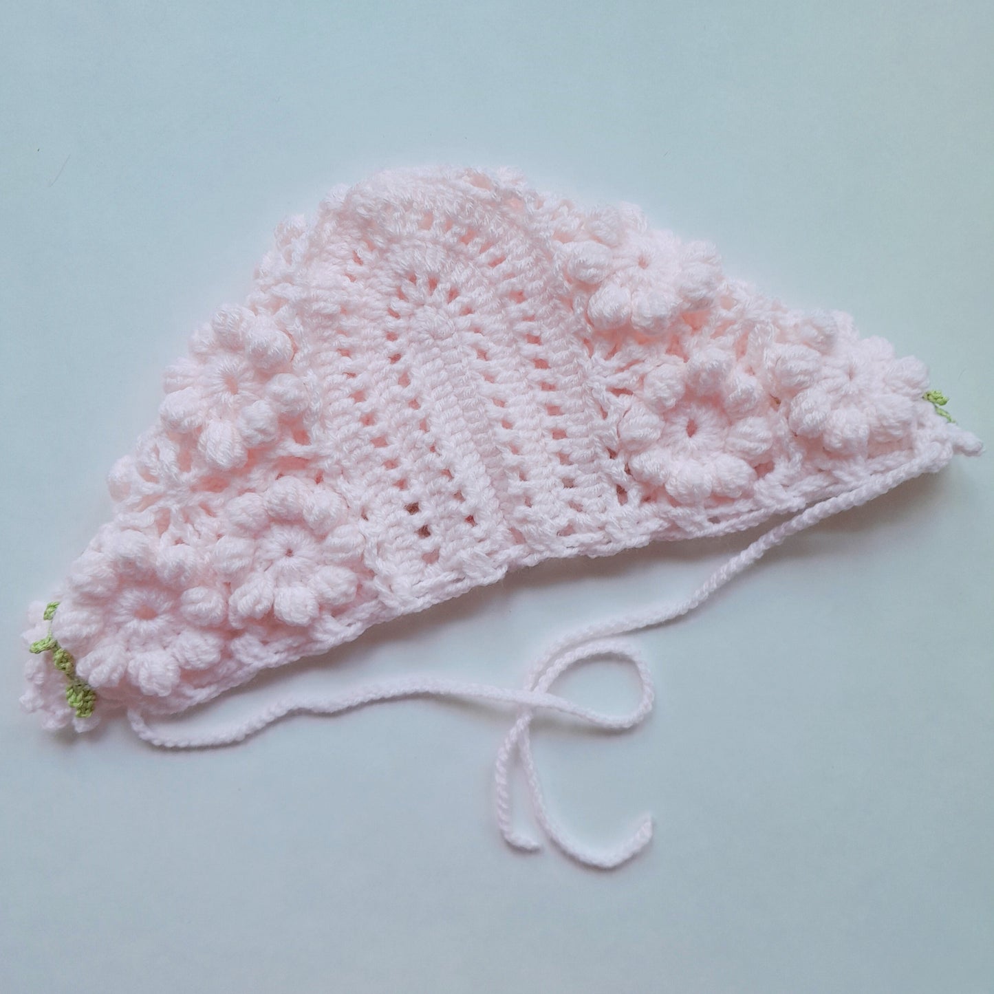 Pink crocheted baby hat on a light blue background