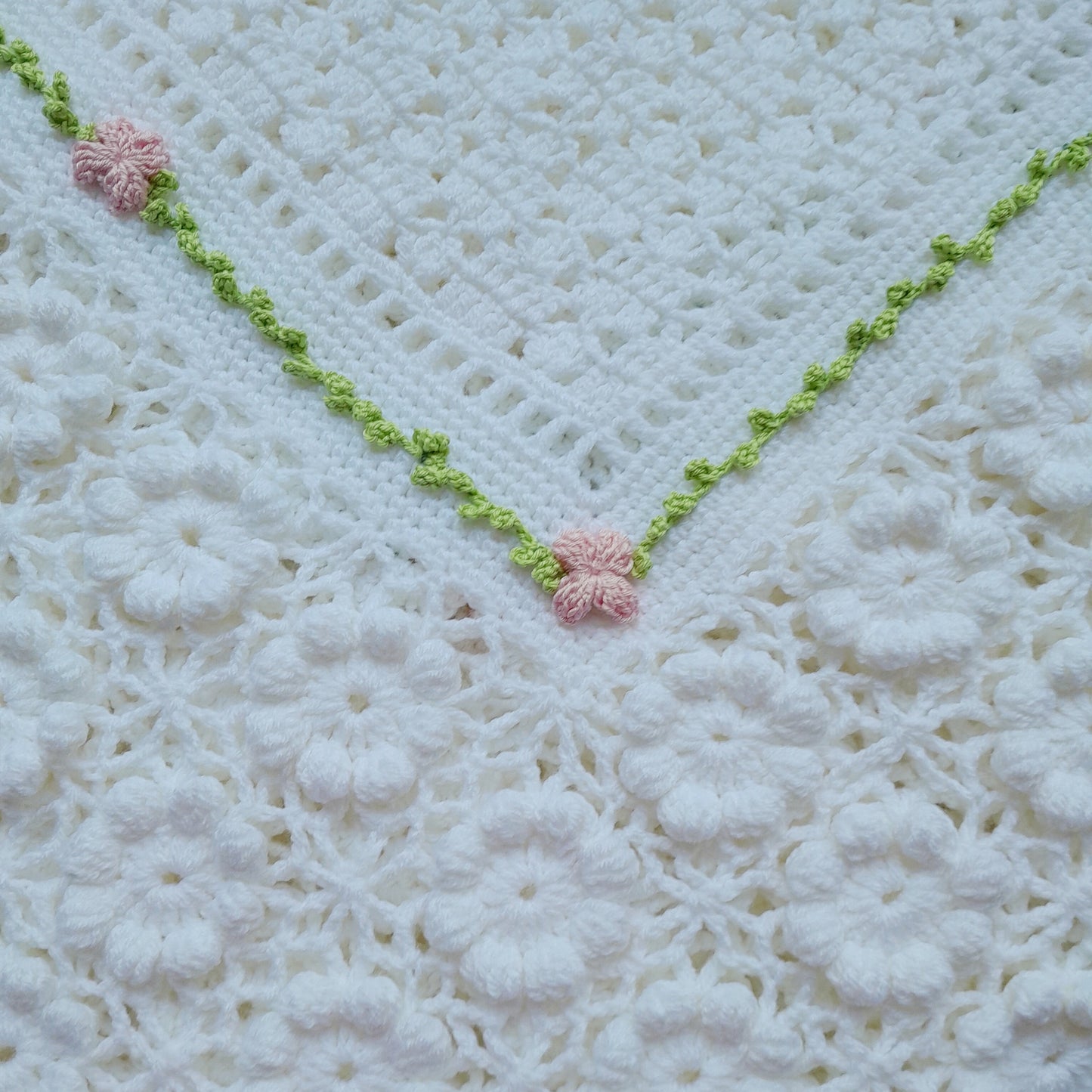 Close-up of a crocheted blanket with pink flowers and green trim on a white background
