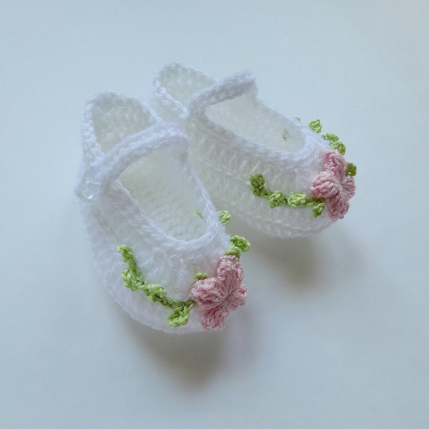 White baby shoes with pink flowers and green accents on a light gray background