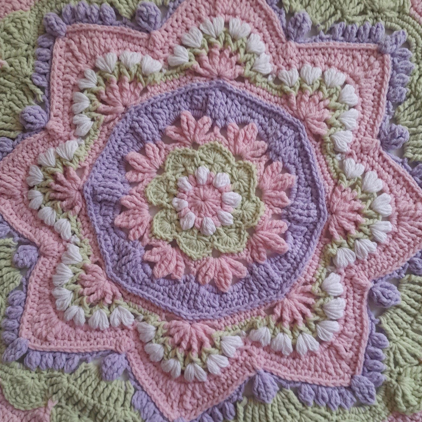 Close-up of a crocheted blanket with a floral pattern in pastel colors.