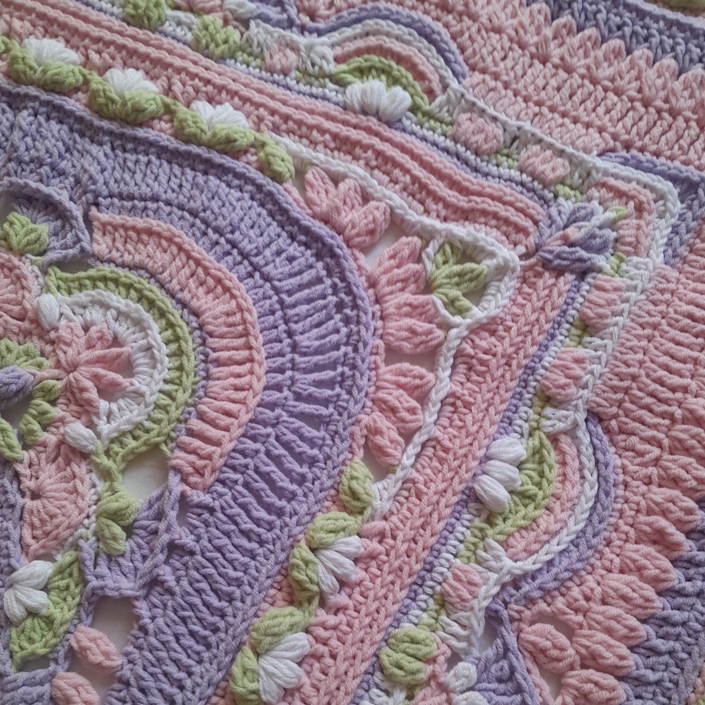 Close-up of a crocheted blanket with intricate patterns in pastel colors.