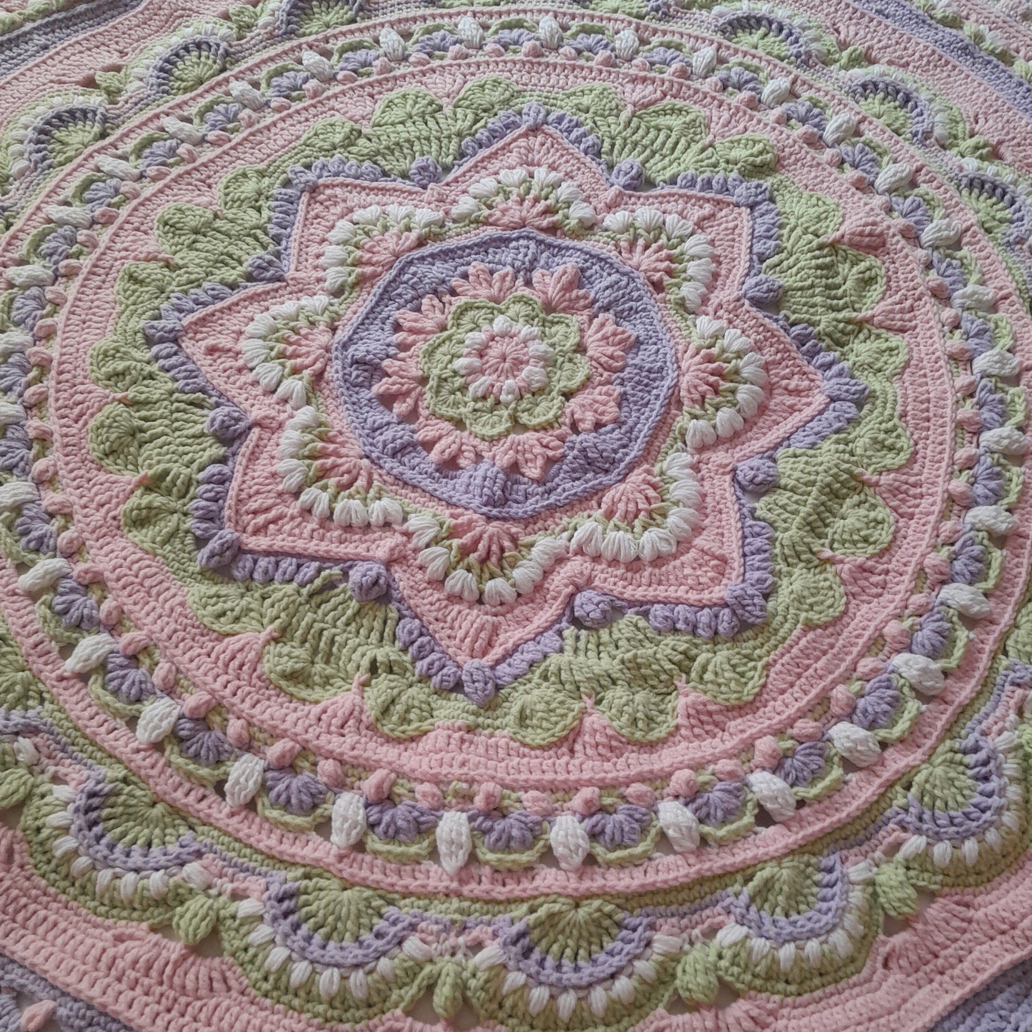 Close-up of a crocheted blanket with a circular pattern in pastel colors.