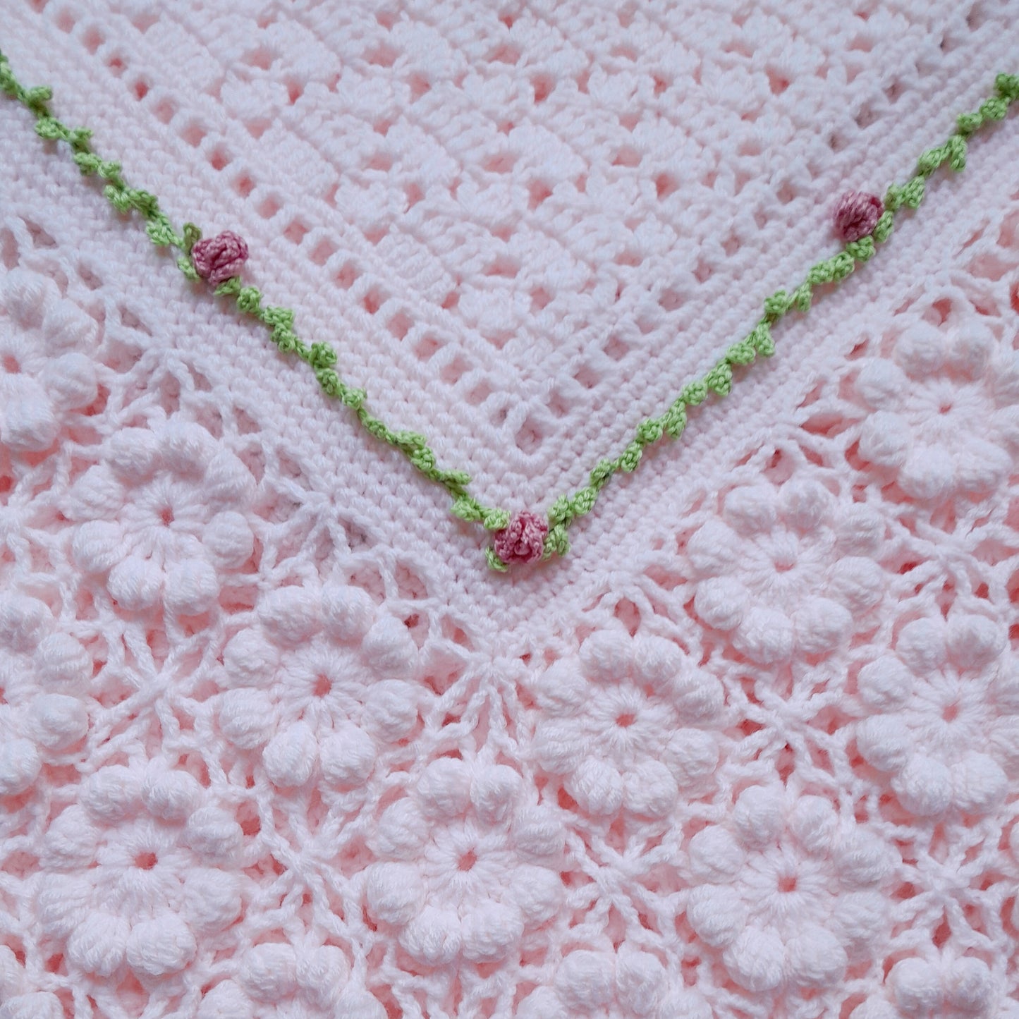Close-up of a pink crocheted blanket with green trim