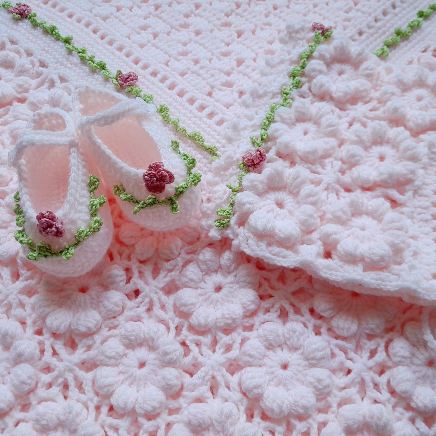 Pink baby booties with green accents on a pink textured blanket
