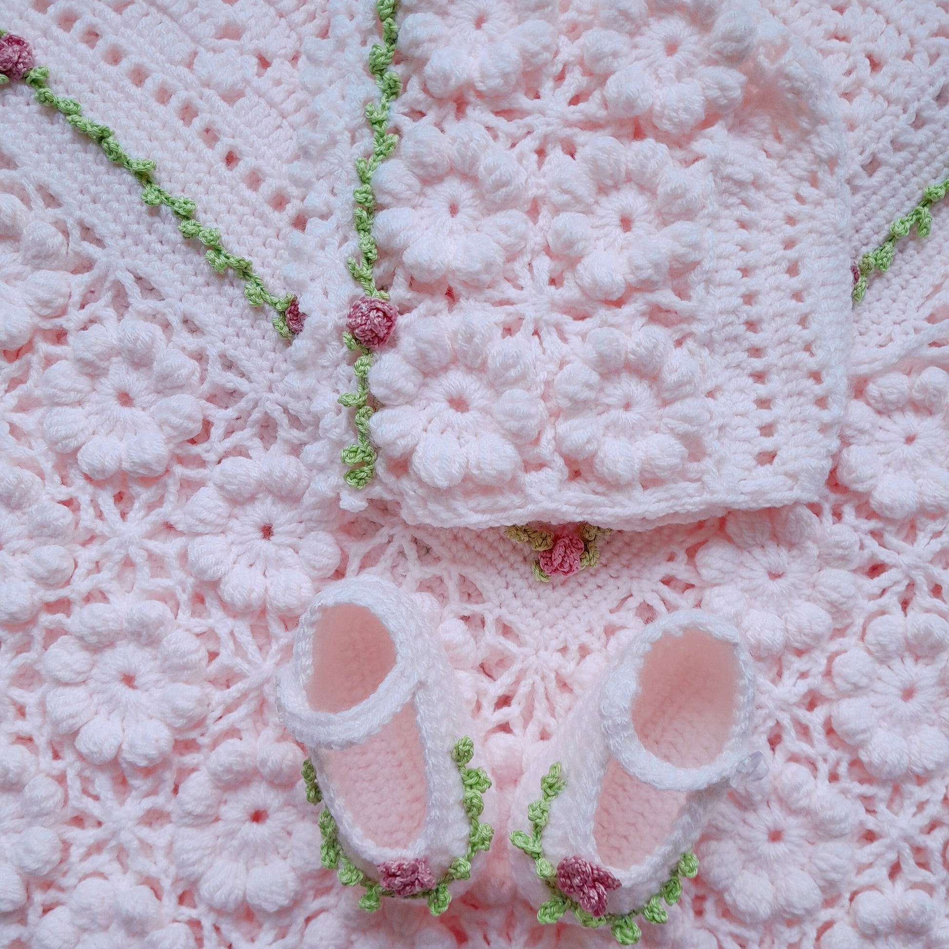 Pink crochet baby blanket with matching booties on a pink textured background