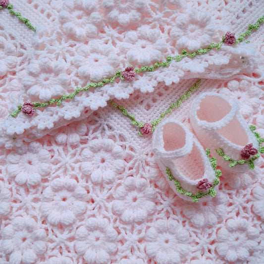 Pink baby booties on a textured pink blanket with green trim
