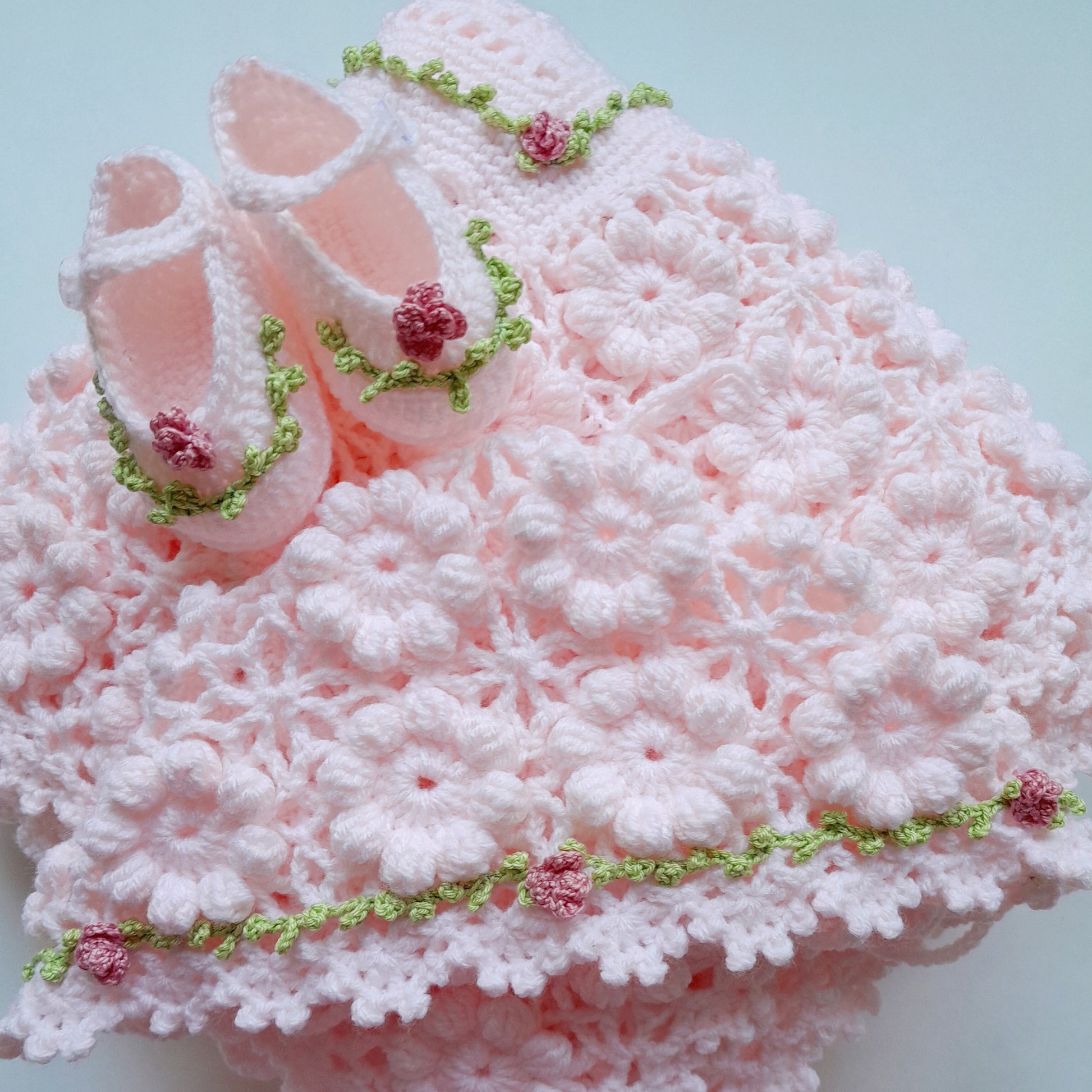 Pink crocheted blanket with baby booties on a light blue background