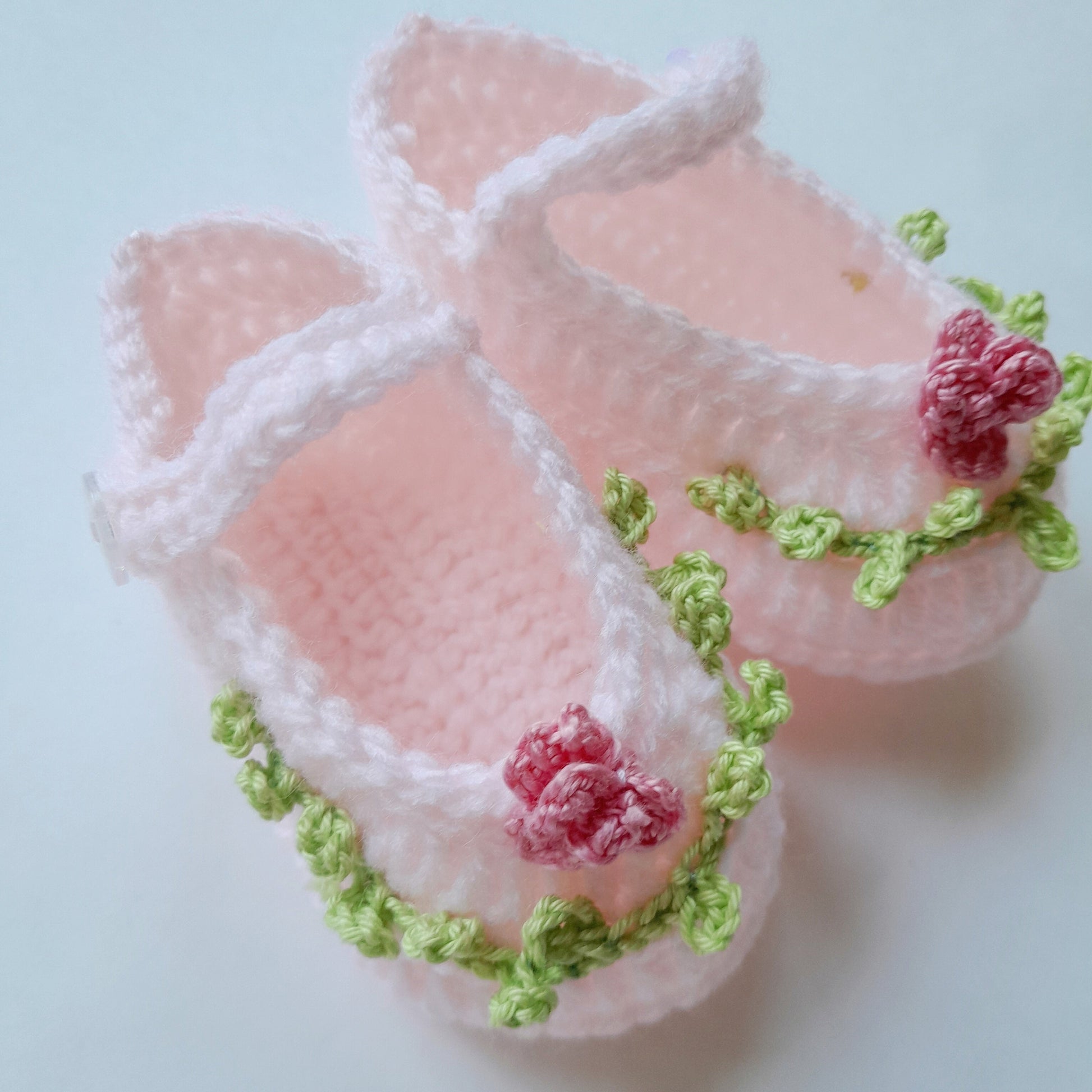 Pink baby shoes with green accents and red flowers on a light blue background