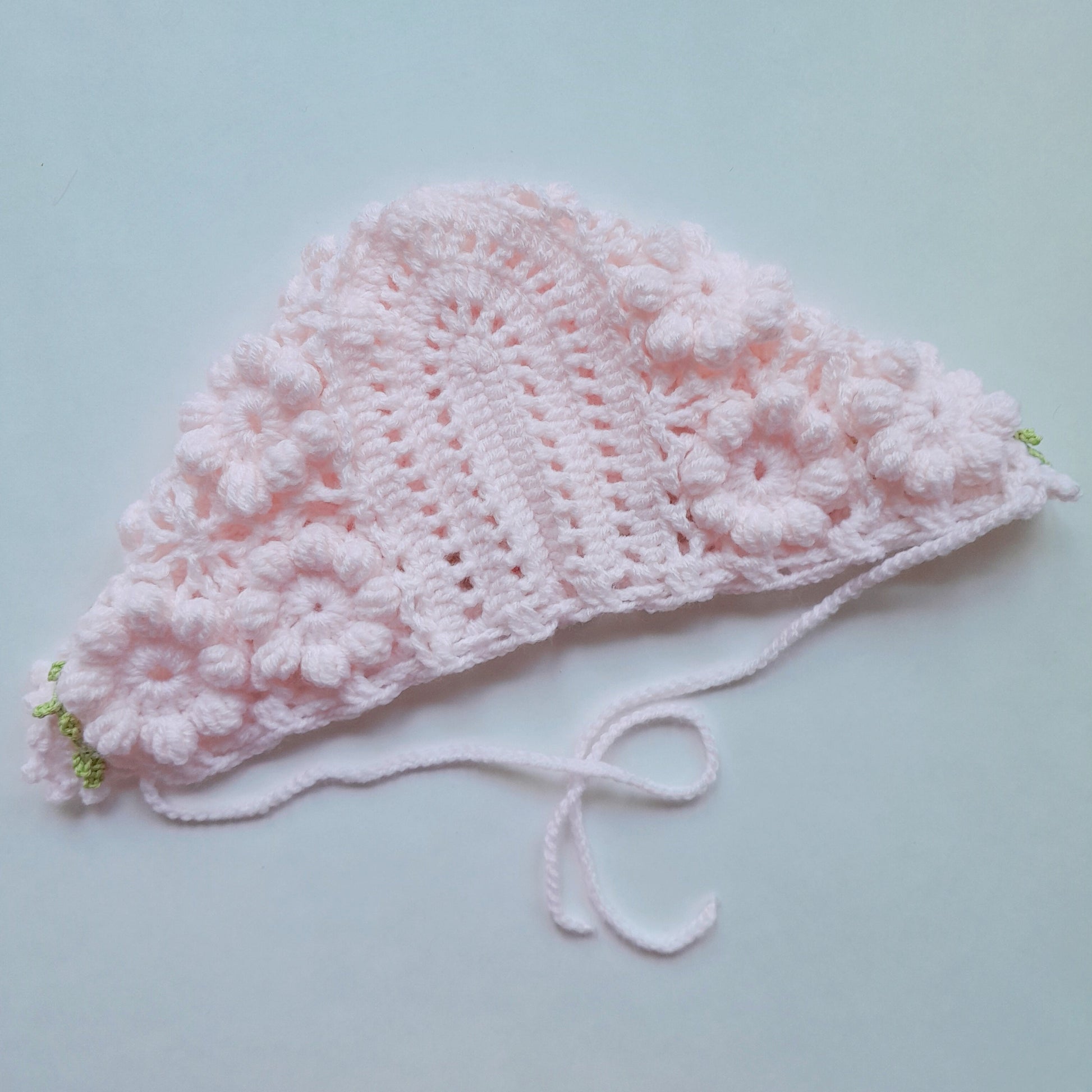 Pink crocheted baby hat on a light blue background