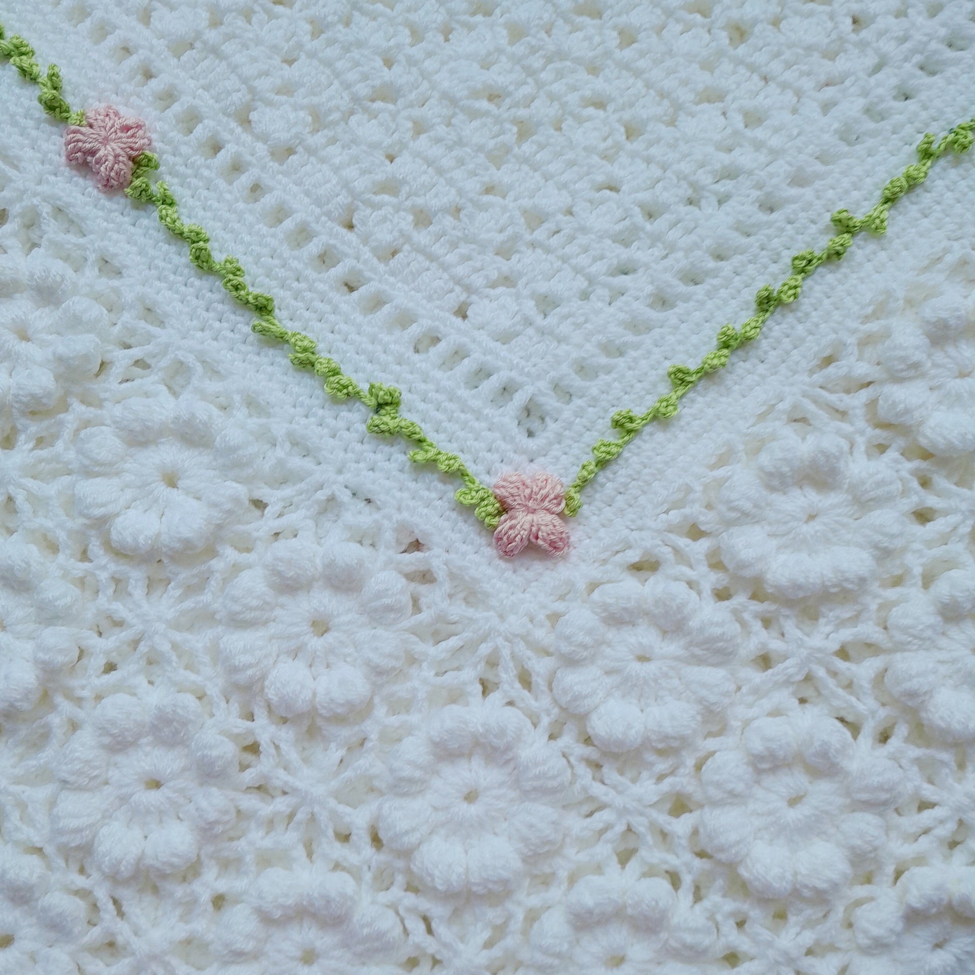 Close-up of a crocheted blanket with pink flowers and green trim on a white background