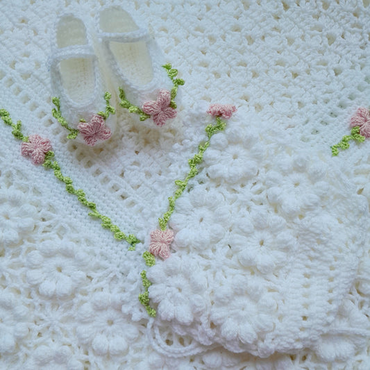 White crocheted blanket with pink flowers and green accents on a textured white background