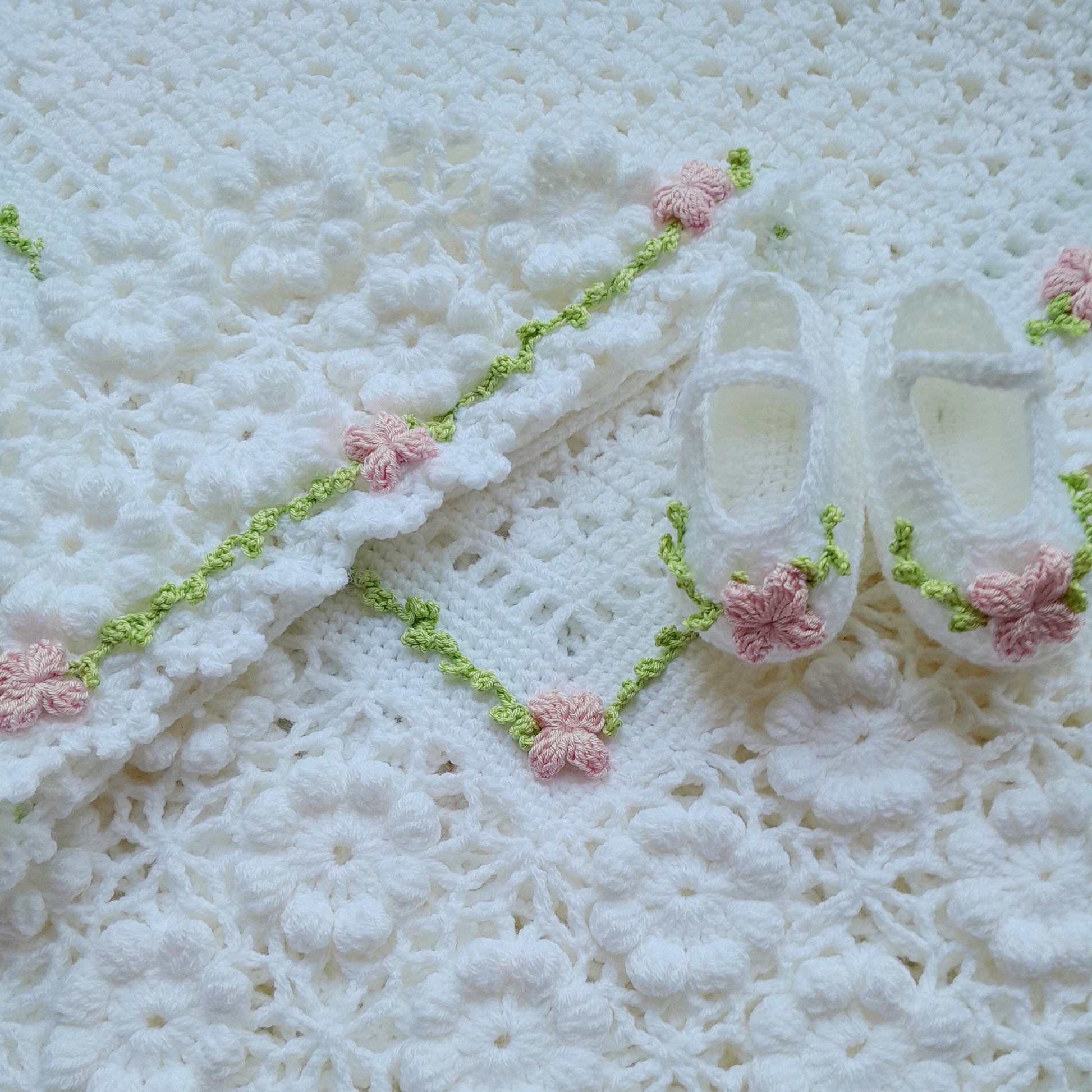 White baby shoes with pink flowers on a textured white background