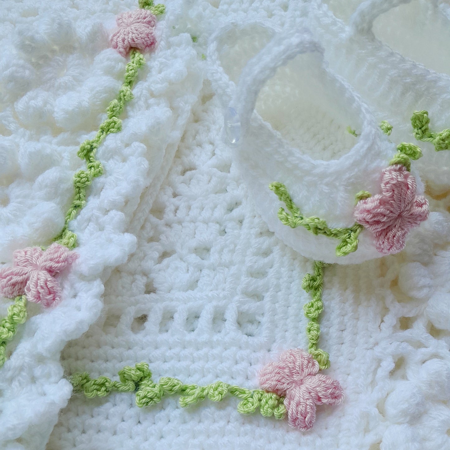 Close-up of a crocheted white fabric with pink flowers and green leaves.