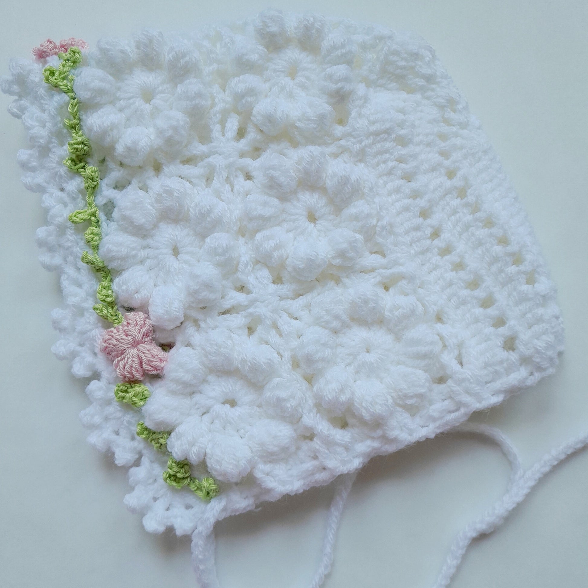 White crocheted baby bonnet with floral details on a light gray background