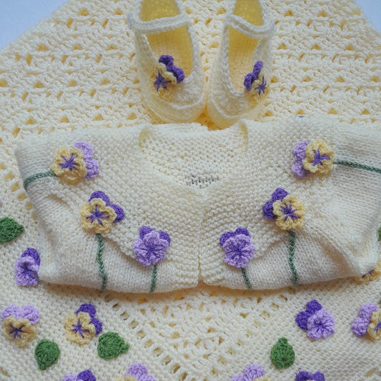 Knitted baby outfit with floral patterns on a matching blanket