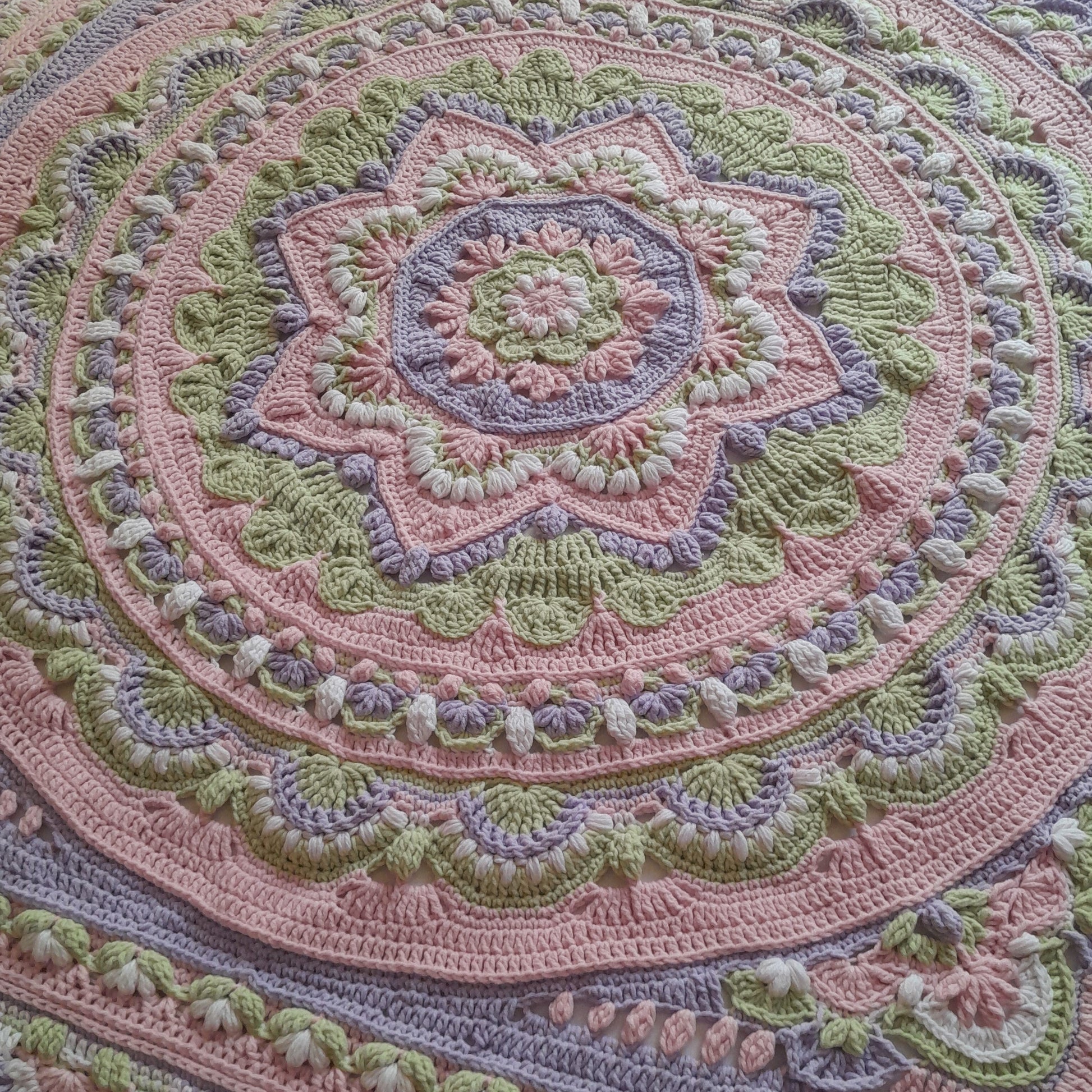 Close-up of a crocheted blanket with intricate patterns in pink, green, and purple.