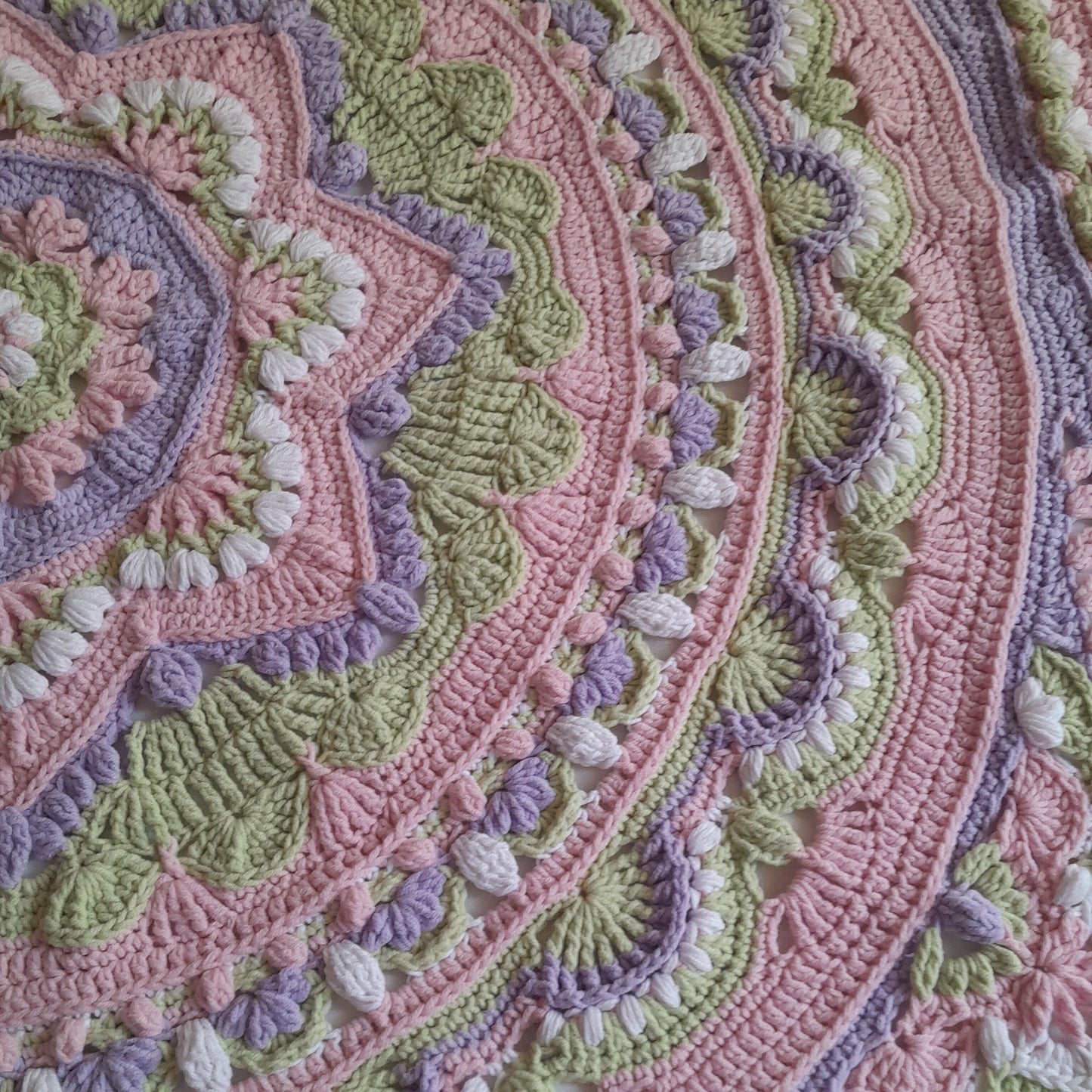 Close-up of a crocheted blanket with pink, green, and purple patterns.