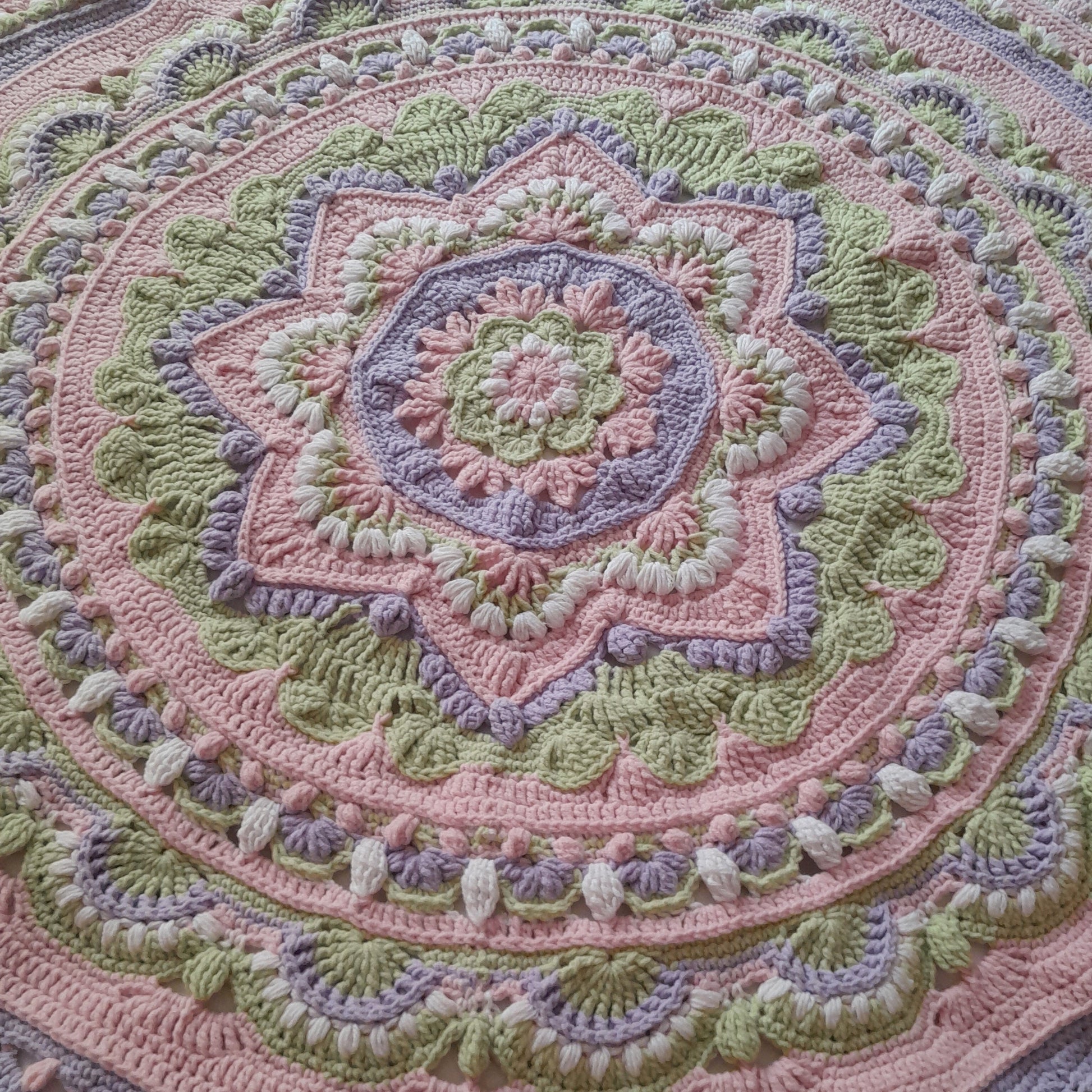 Close-up of a crocheted blanket with a circular pattern in pastel colors.