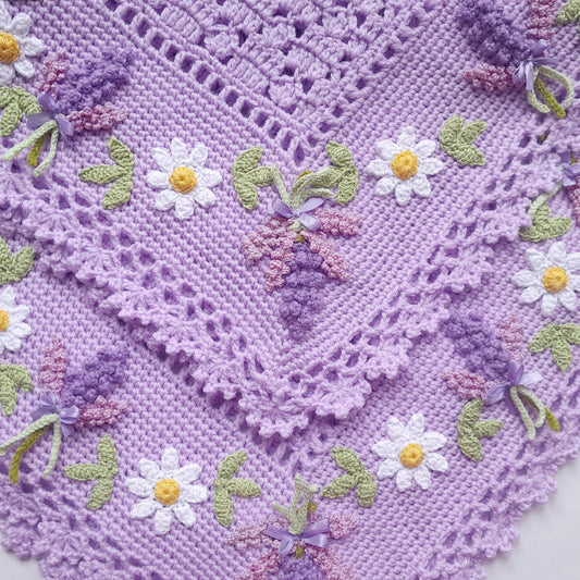 Purple crocheted blanket with floral embroidery on a white background